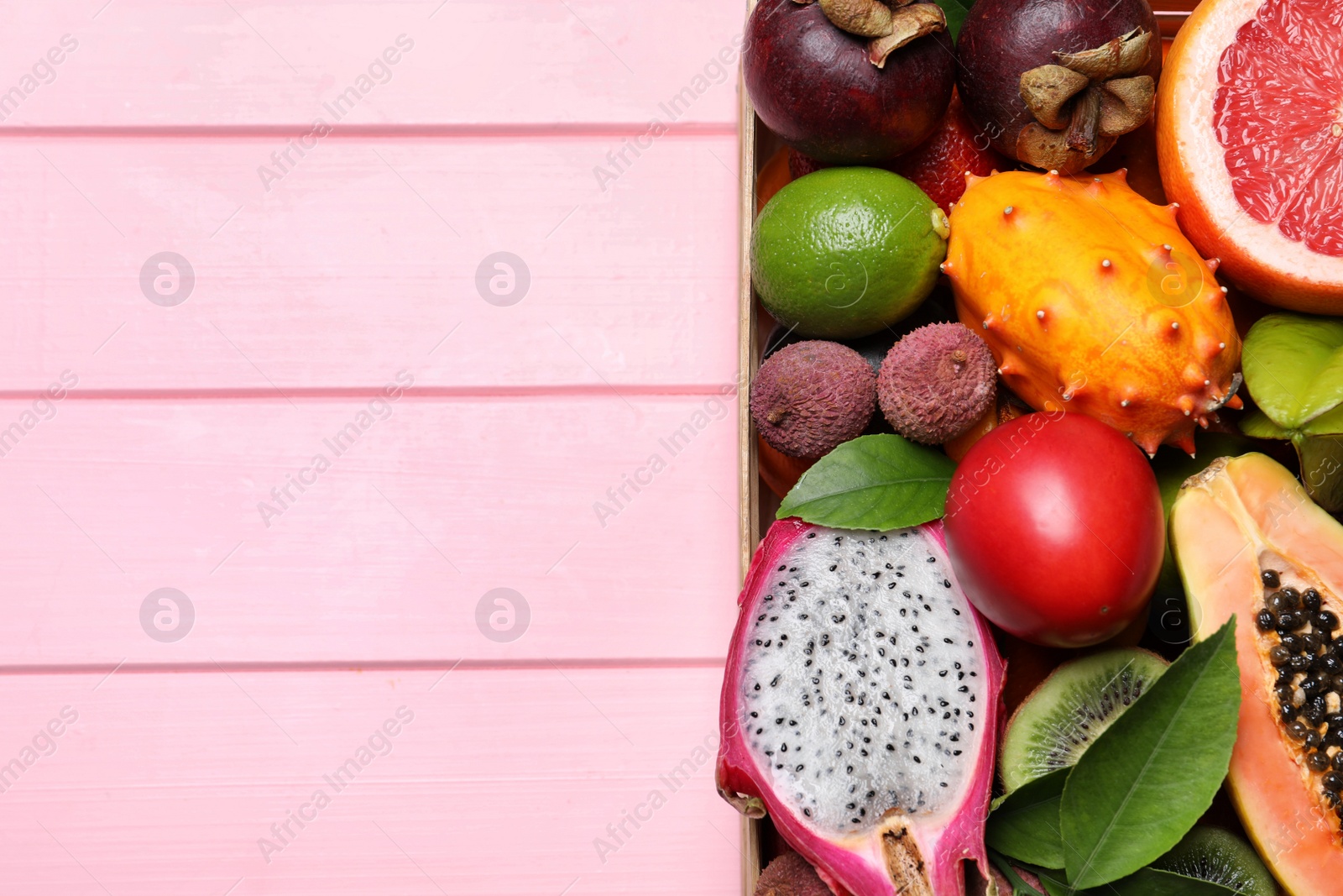 Photo of Different tropical fruits in box on pink wooden background, top view. Space for text