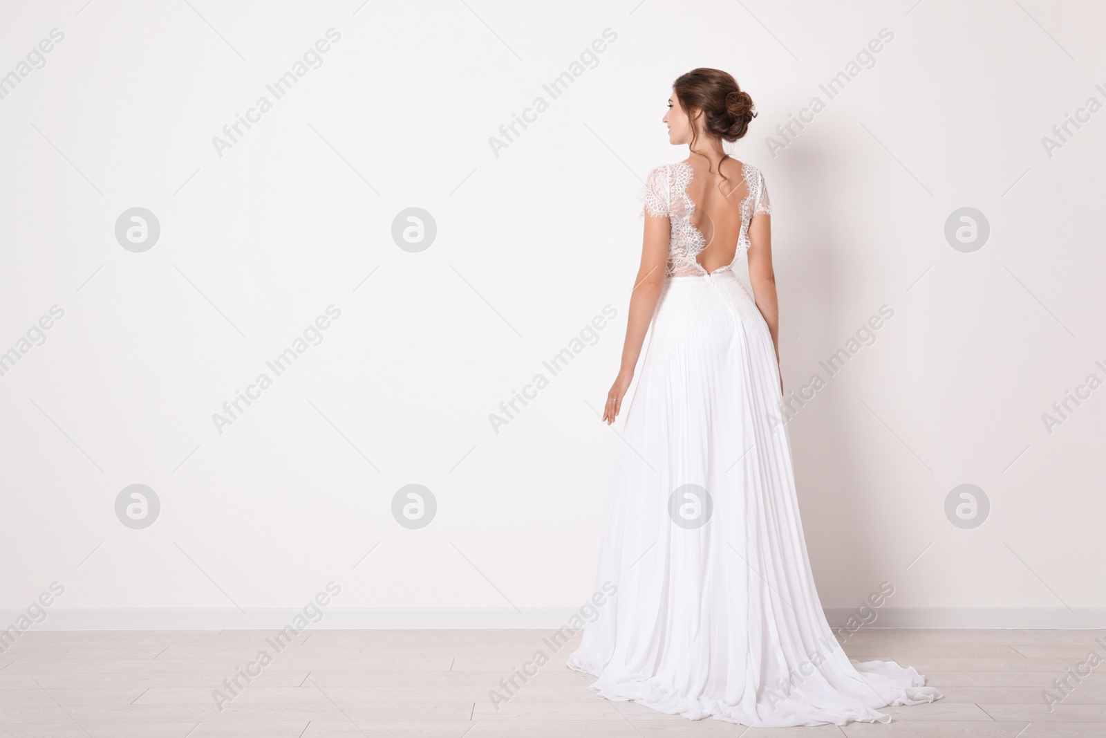 Photo of Young bride wearing beautiful wedding dress near light wall. Space for text