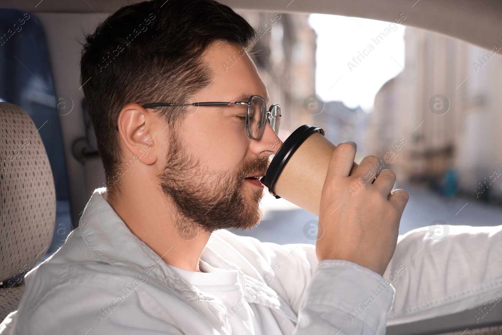 Photo of To-go drink. Handsome man drinking coffee in car