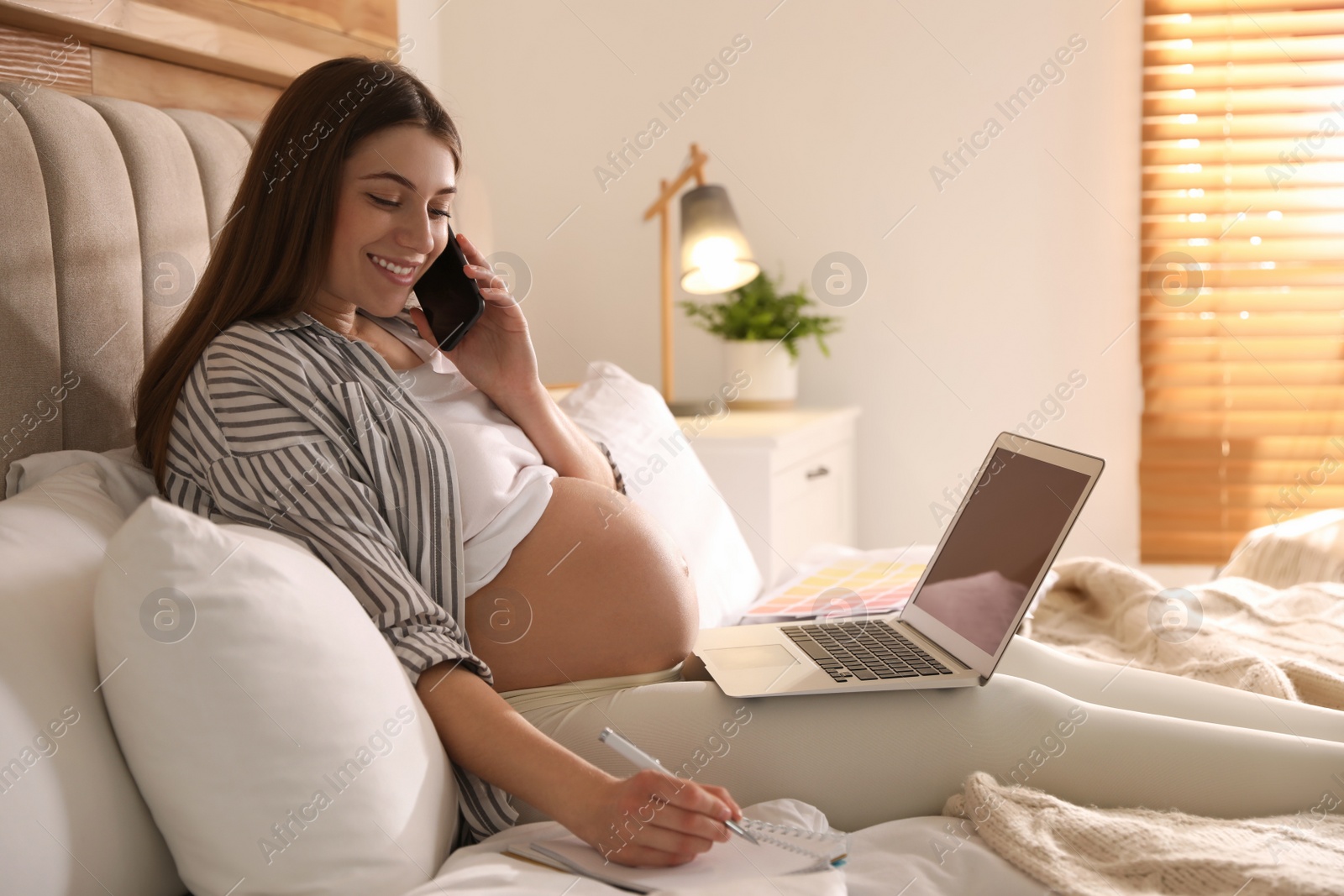 Photo of Pregnant woman working on bed at home. Maternity leave