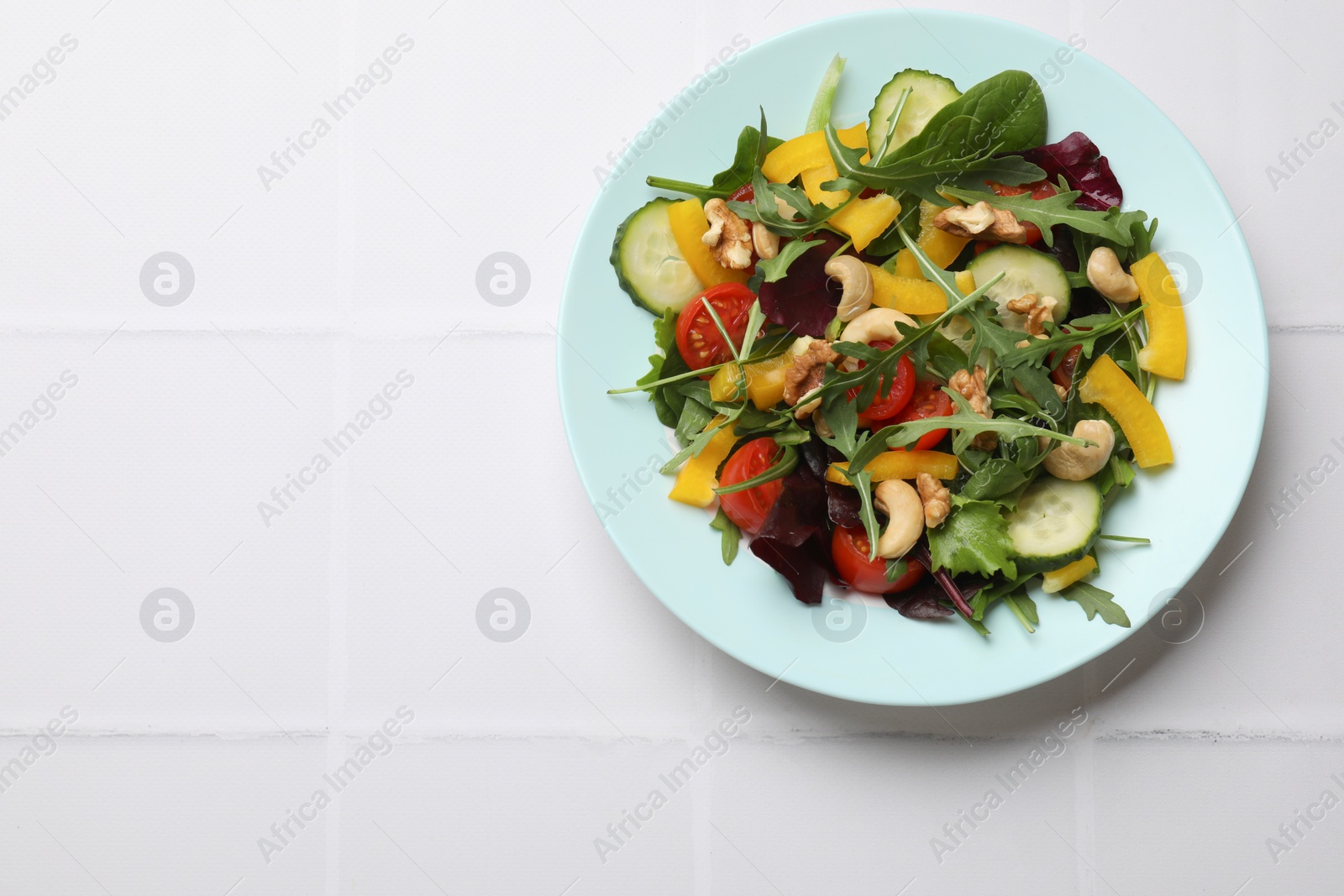 Photo of Tasty fresh vegetarian salad on white tiled table, top view. Space for text