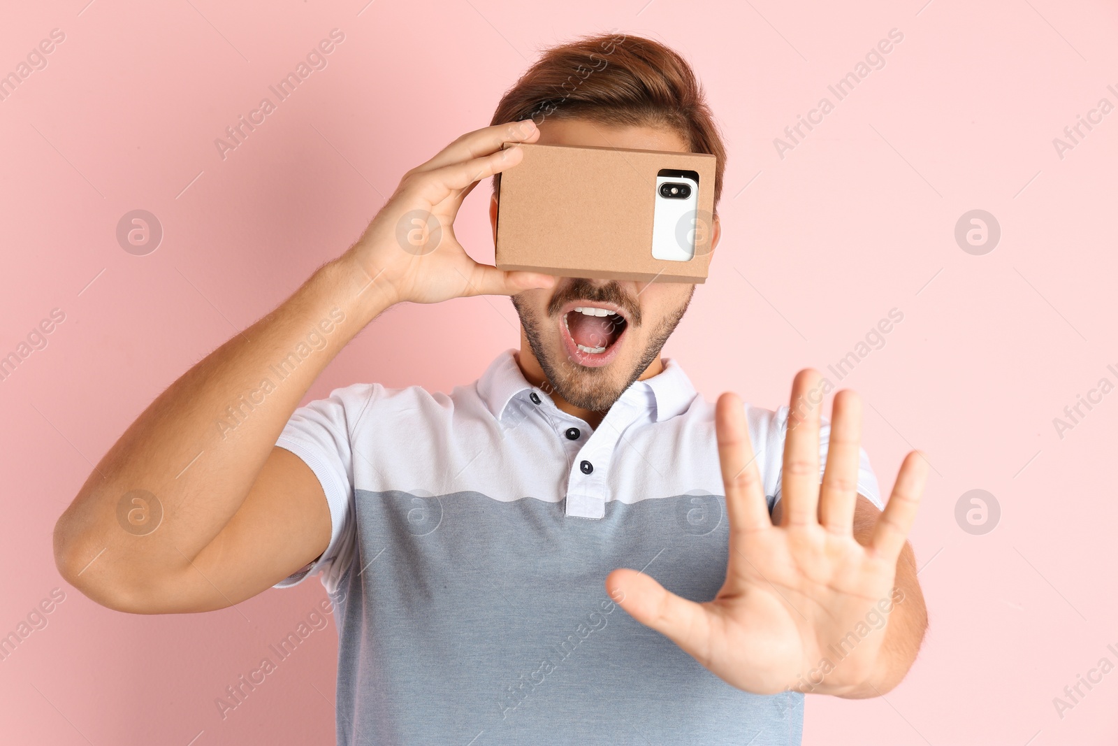 Photo of Young man using cardboard virtual reality headset on color background