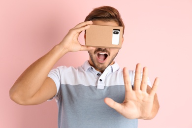 Young man using cardboard virtual reality headset on color background