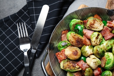 Delicious Brussels sprouts with bacon served on grey table, flat lay