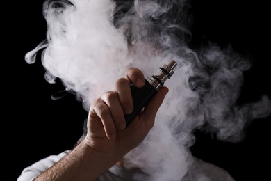 Man using electronic cigarette against black background, focus on hand