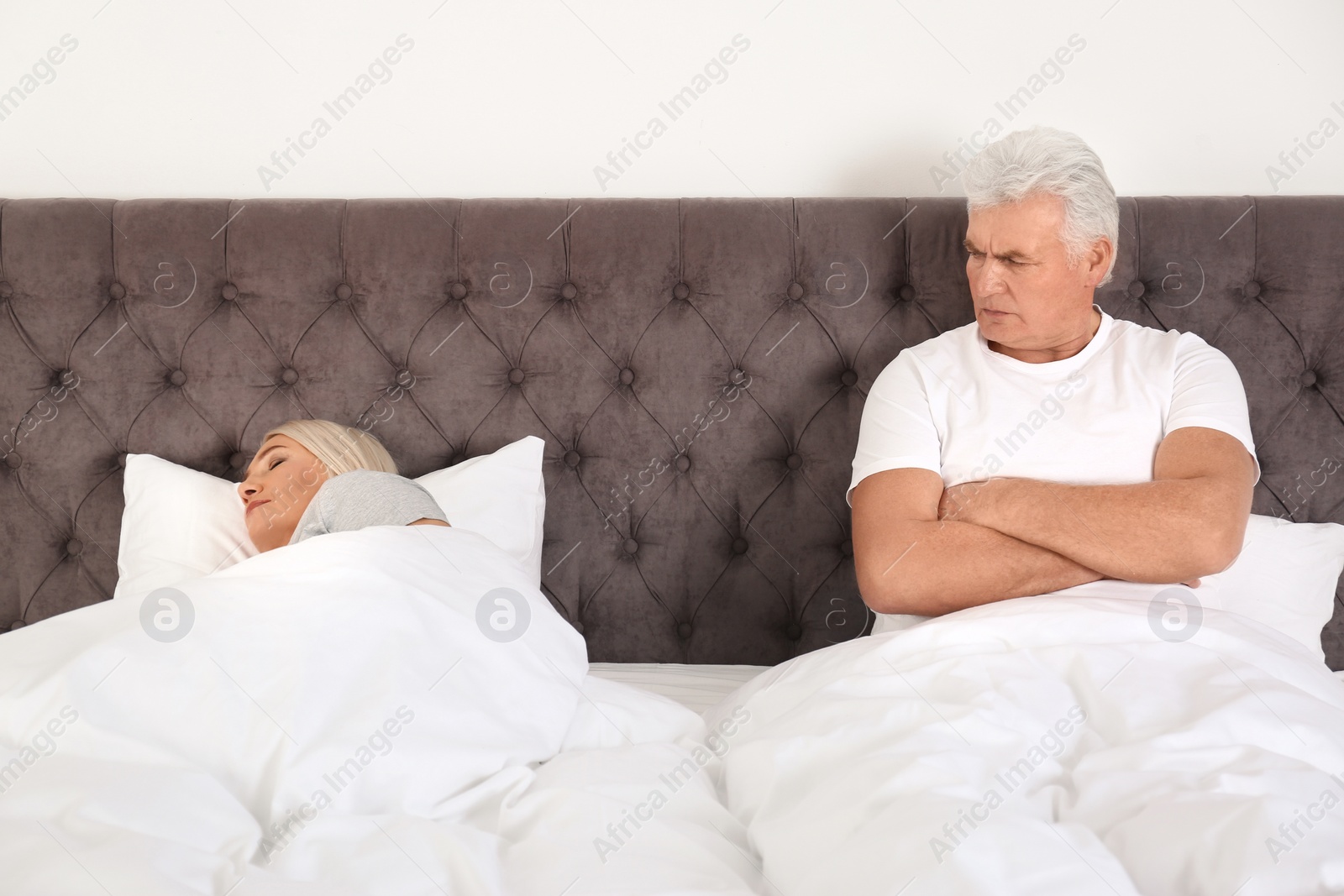 Photo of Upset mature man sitting on bed near his sleeping wife at home. Relationship problems