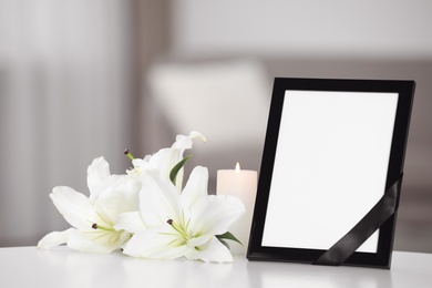 Photo of Funeral photo frame with black ribbon and lilies on white table indoors. Space for design