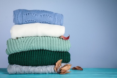 Photo of Stack of folded knitted sweaters and autumn leaves on blue wooden table against grey background. Space for text