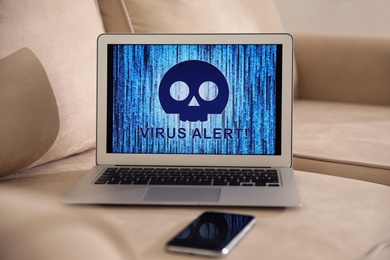 Photo of Smartphone and laptop with warning about virus attack on beige sofa