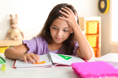 Emotional little girl doing homework at table indoors