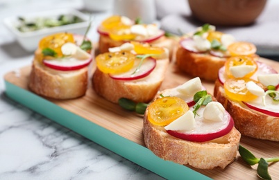 Photo of Tasty bruschettas with radish and yellow cherry tomatoes on white marble table, closeup