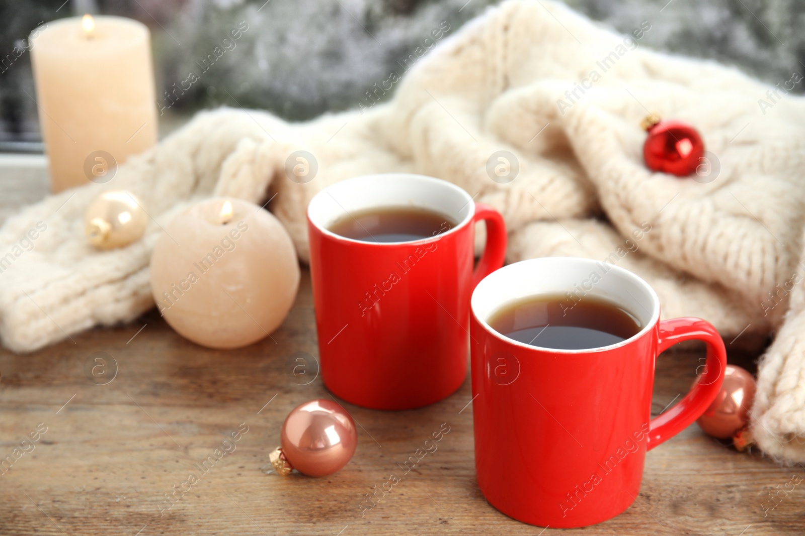 Photo of Cups of hot winter drink with knitted sweater on window sill indoors