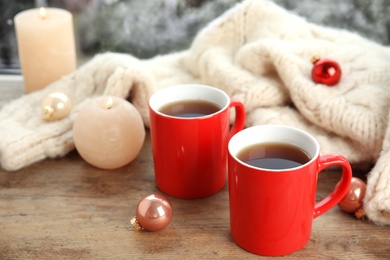 Photo of Cups of hot winter drink with knitted sweater on window sill indoors