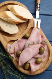 Slices of delicious ham with olives and baguette served on blue wooden table, flat lay