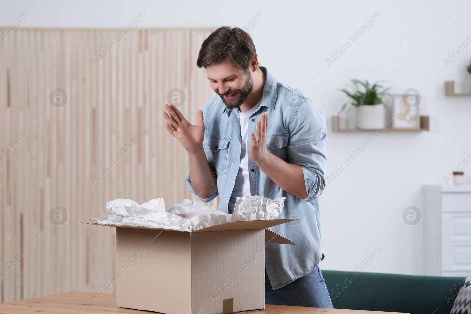 Photo of Emotional man opening parcel at home. Internet shopping