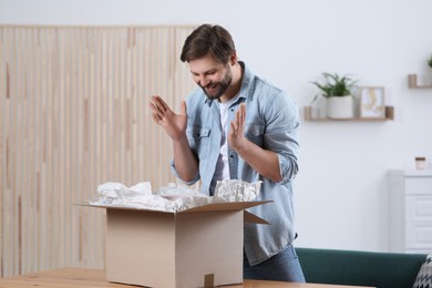 Photo of Emotional man opening parcel at home. Internet shopping