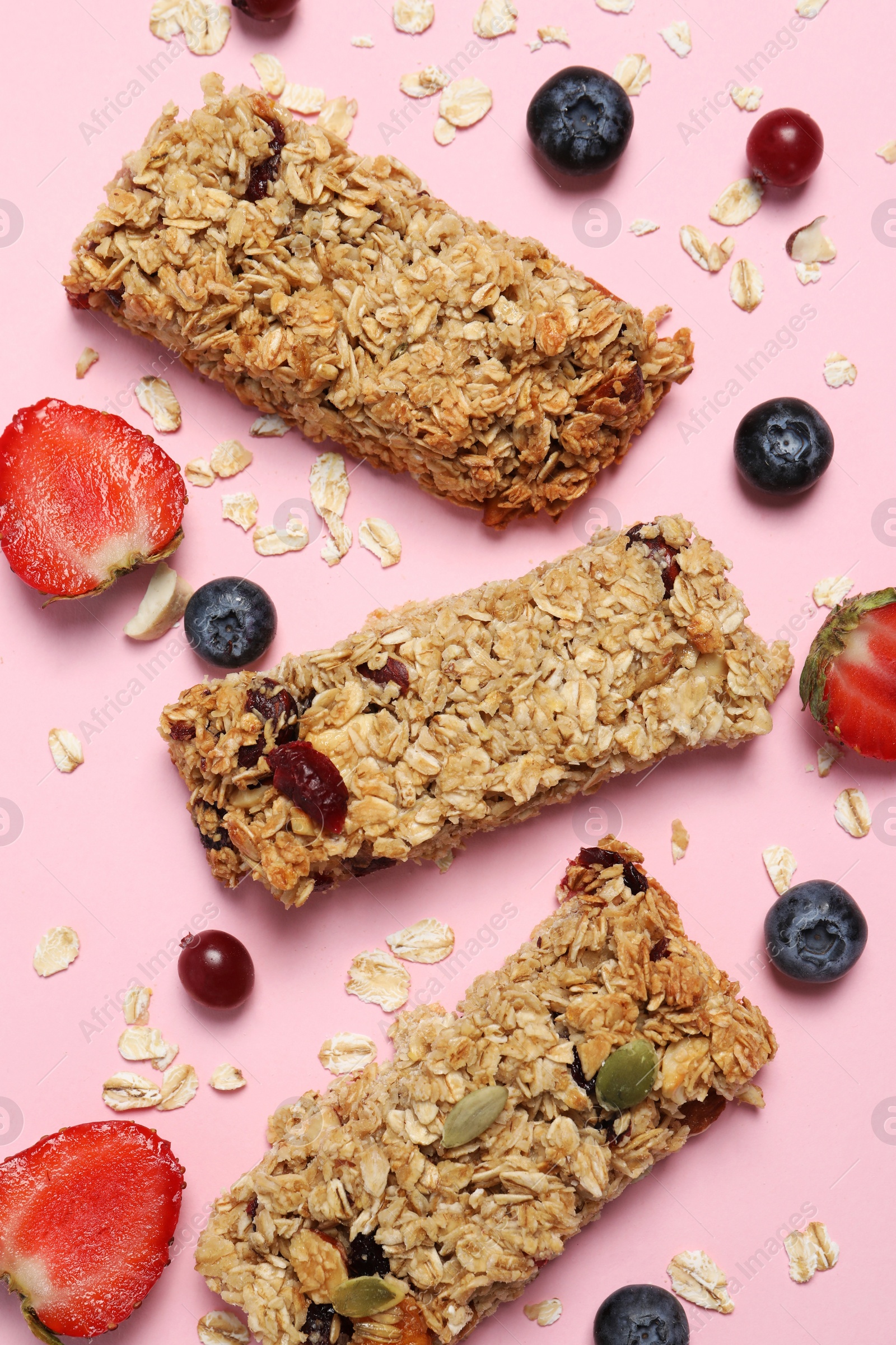 Photo of Tasty granola bars and ingredients on pink background, flat lay
