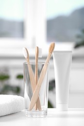 Photo of Bamboo toothbrushes in holder, toothpaste and towel on white table indoors