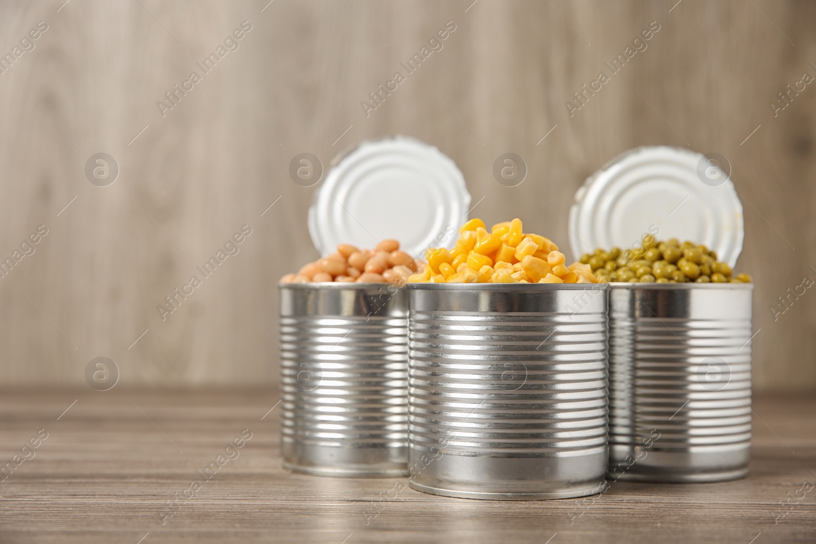 Photo of Open tin cans with conserved vegetables on wooden table. Space for text