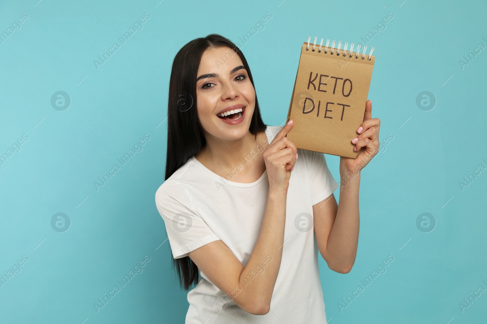 Photo of Happy woman holding notebook with words Keto Diet on turquoise background