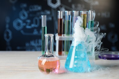 Photo of Laboratory glassware with colorful liquids and steam on white wooden table against black background. Chemical reaction