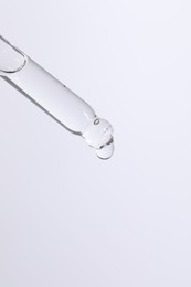 Dripping cosmetic serum from pipette on white background