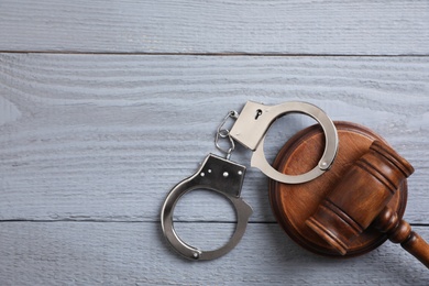 Flat lay composition with handcuffs and gavel on grey wooden table, space for text. Criminal law