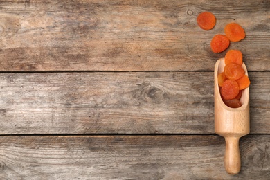 Photo of Scoop of dried apricots on wooden background, top view with space for text. Healthy fruit