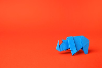 Photo of Origami art. Handmade light blue paper rhinoceros on orange background, space for text
