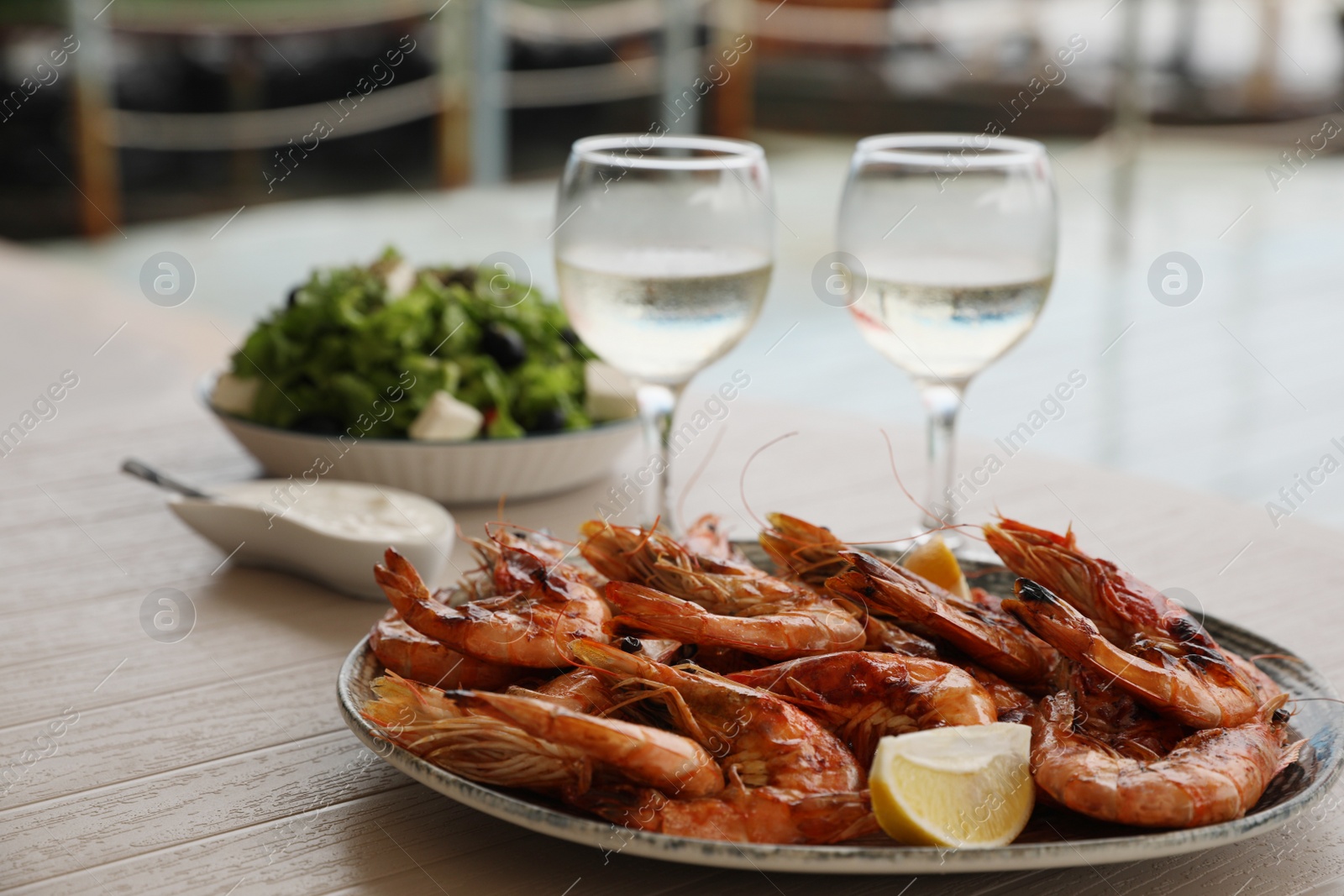 Photo of Plate of delicious cooked shrimps served with lemon and wine at table outdoors