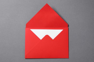 Blank sheet of paper in open letter envelope on grey background, top view