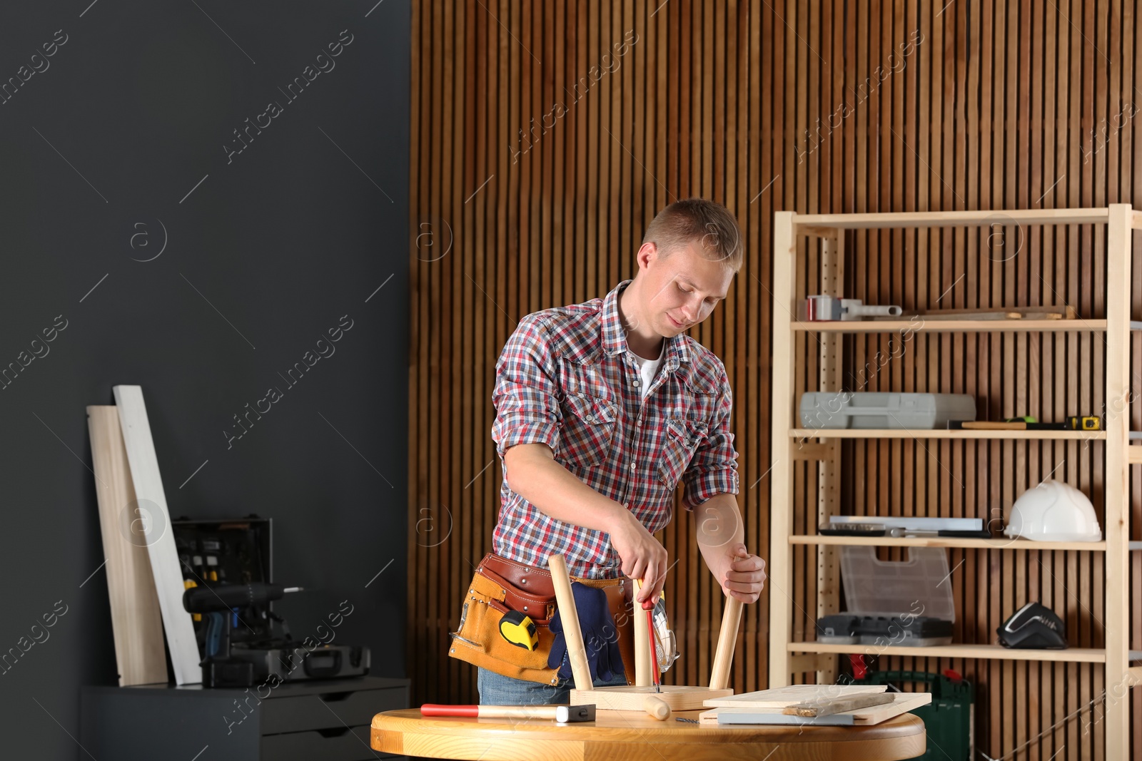 Photo of Handsome young working man repairing wooden stool using screwdriver indoors