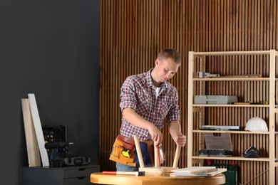 Handsome young working man repairing wooden stool using screwdriver indoors