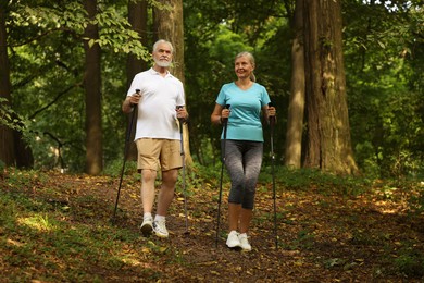 Photo of Senior man and woman performing Nordic walking in forest. Low angle view