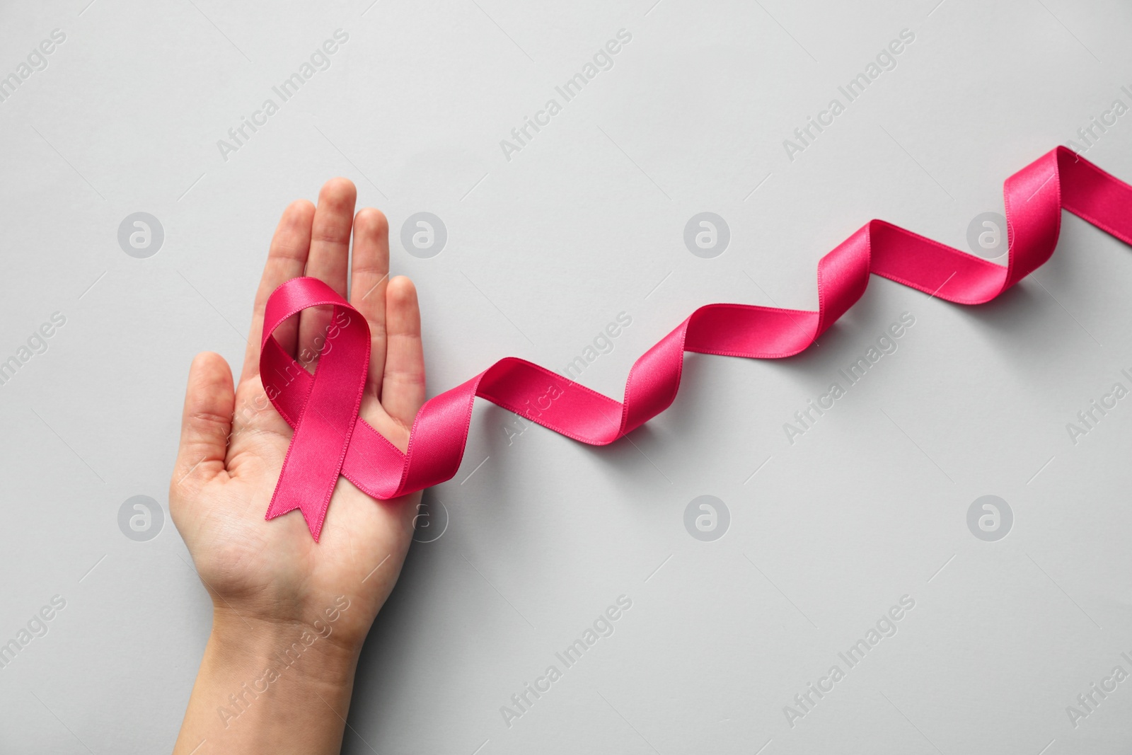 Photo of Woman holding pink ribbon on light grey background, top view. Breast cancer awareness concept