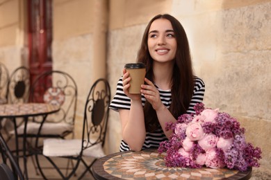 Beautiful woman with bouquet of spring flowers and coffee in outdoor cafe, space for text