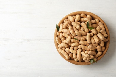 Photo of Bowl with peanuts in shell and space for text on wooden table, top view