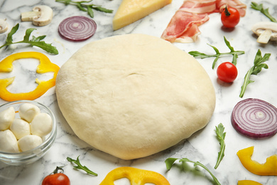 Photo of Dough and fresh ingredients for pizza on white marble table