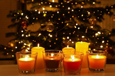 Beautiful burning candles on table in room with Christmas tree. Cozy winter