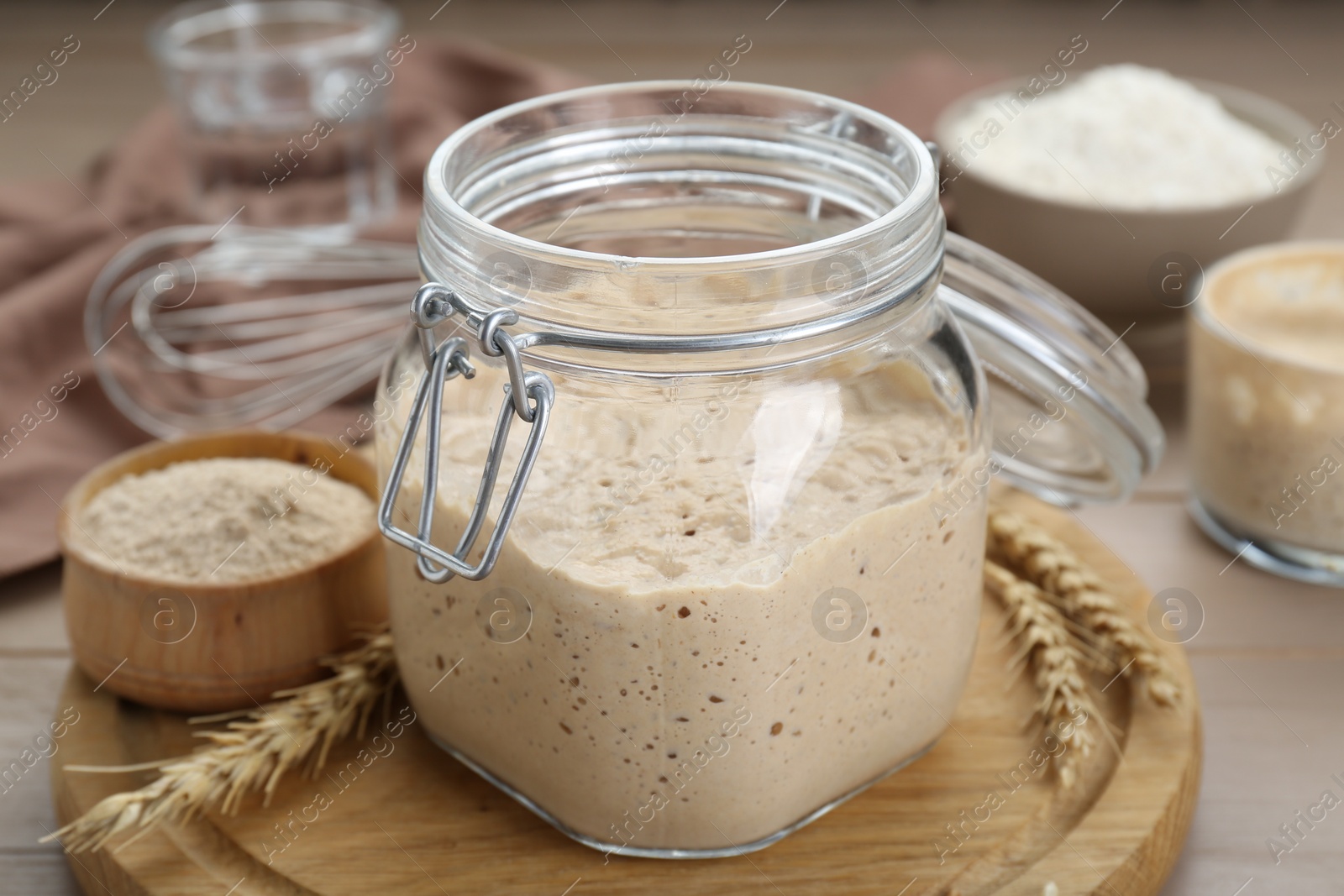 Photo of Leaven and ears of wheat on beige wooden table