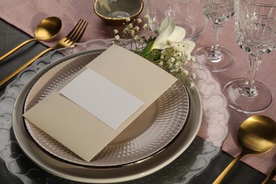 Photo of Stylish table setting. Dishes, cutlery, blank card and floral decor, closeup