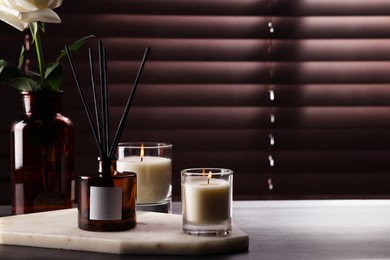 Photo of Aromatic reed air freshener and burning candles on white windowsill, space for text