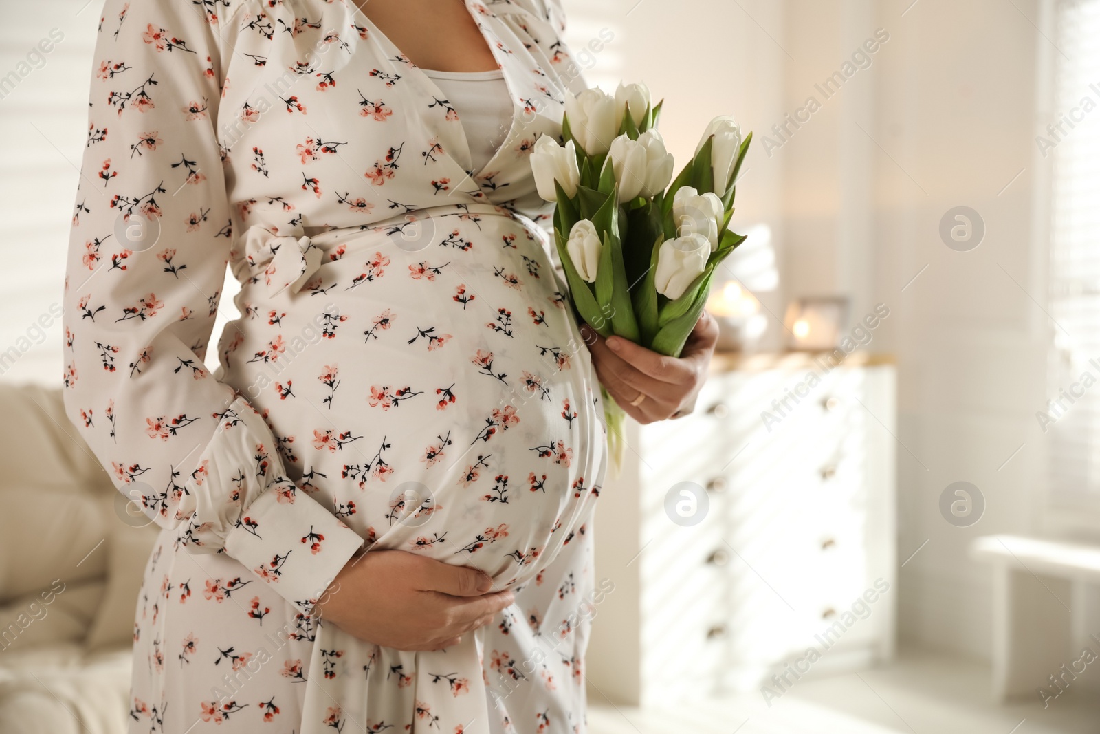 Photo of Young pregnant woman with flowers at home, closeup