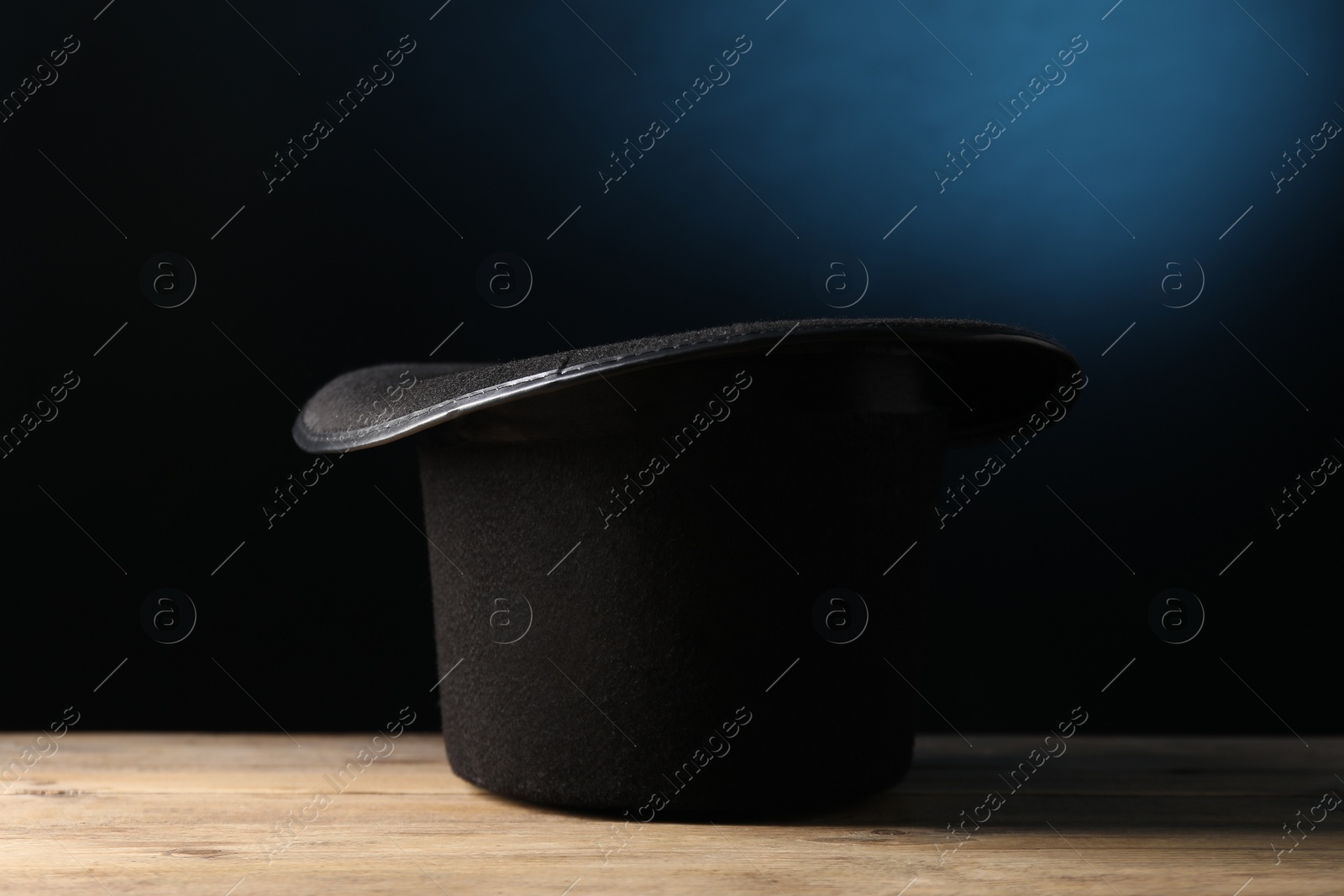 Photo of Magician's hat on wooden table against dark background