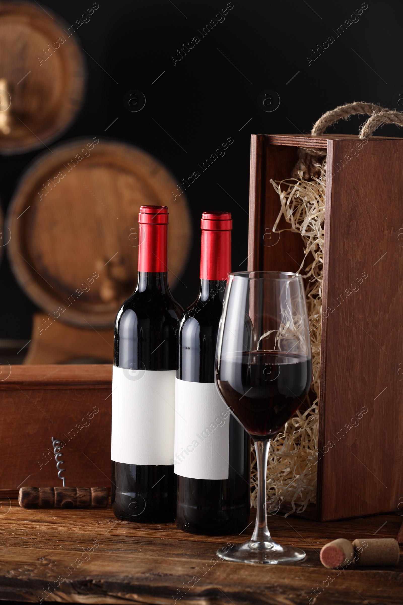 Photo of Wooden boxes, glass, corkscrew and wine bottles on table against black background