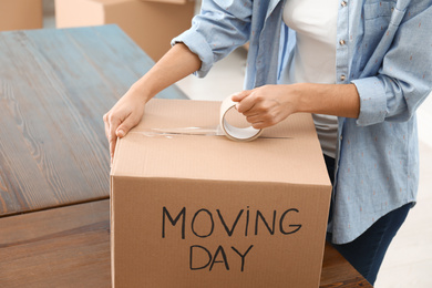 Photo of Woman packing box with words MOVING DAY at wooden table, closeup