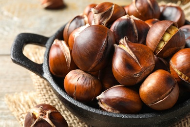 Photo of Tasty roasted edible chestnuts in frying pan on table, closeup