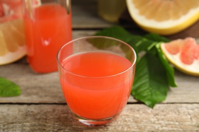 Photo of Glass of pink pomelo juice with green leaves on wooden table, closeup