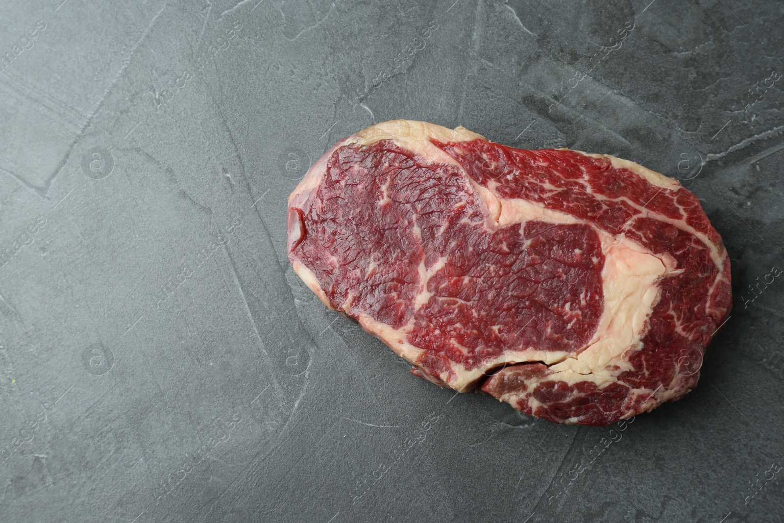 Photo of Piece of raw beef meat on grey table, top view. Space for text