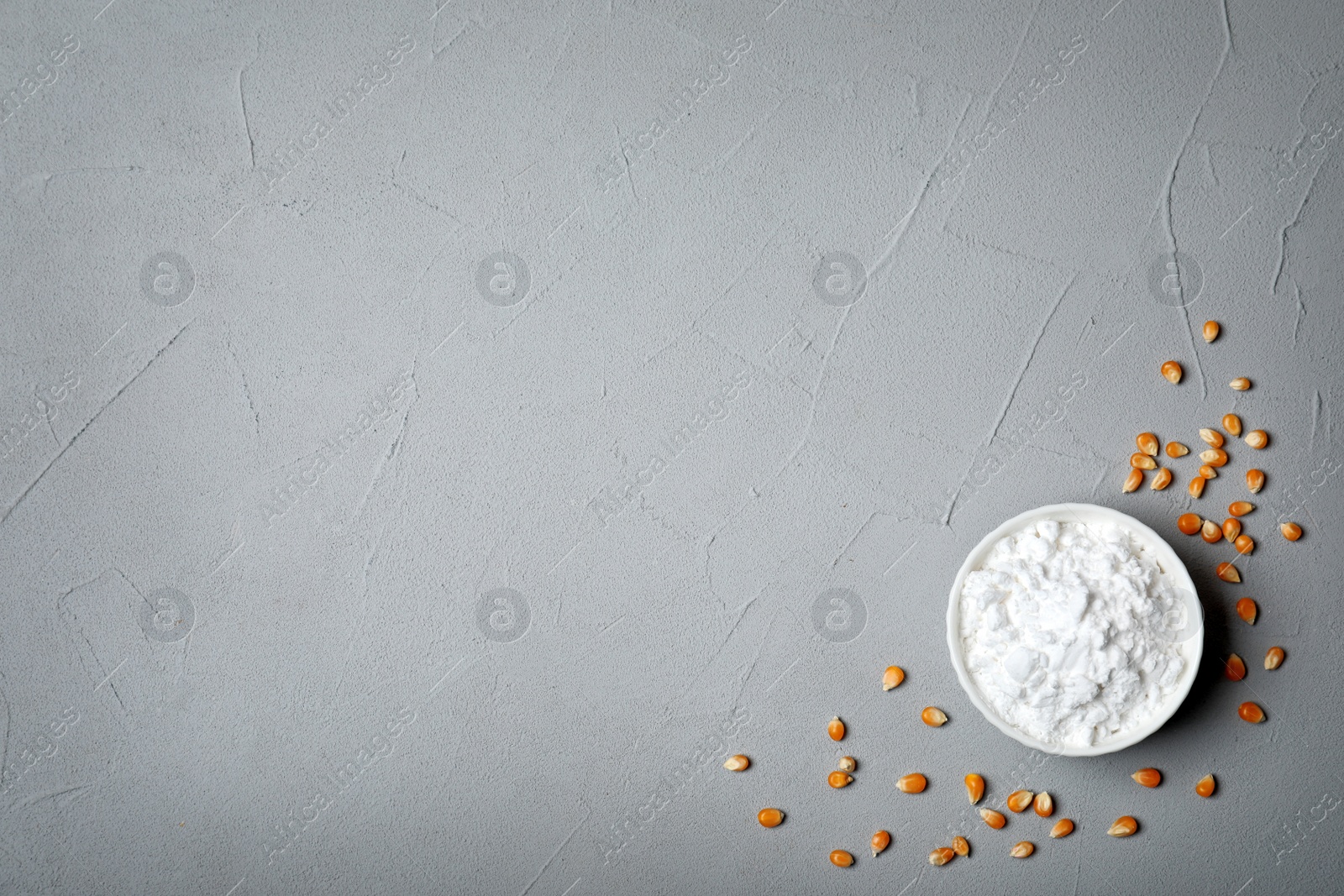 Photo of Bowl with corn starch, kernels and space for text on grey background, top view